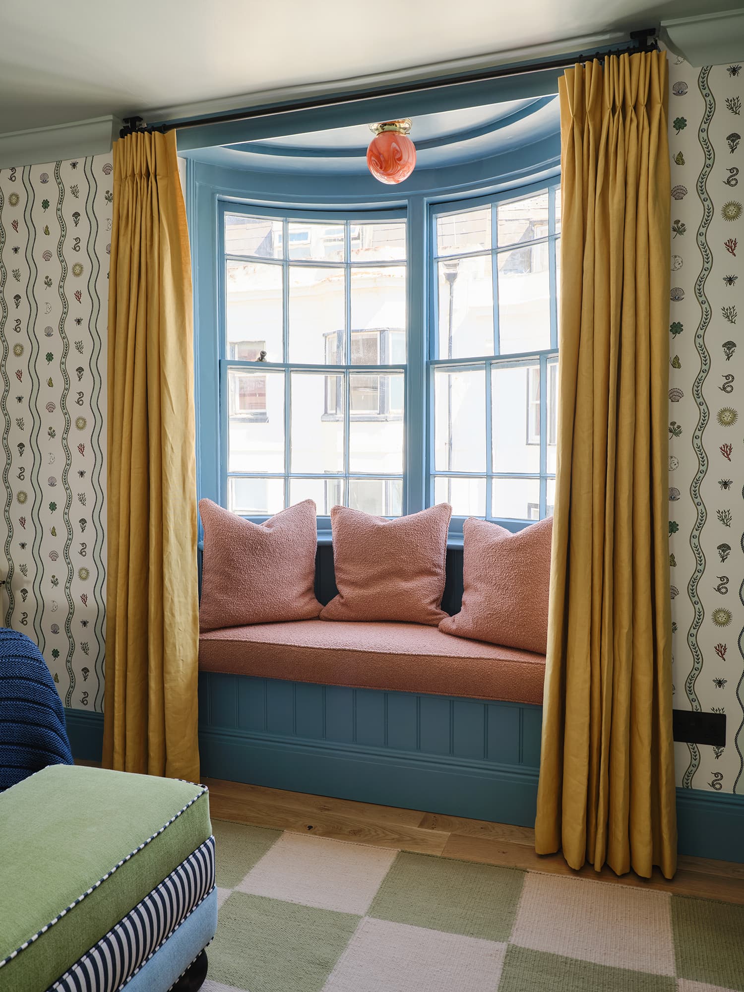 Cozy room with a window seat, pink cushions, yellow curtains, and patterned wallpaper.